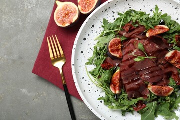 Plate of tasty bresaola salad with figs, sun-dried tomatoes, balsamic vinegar and fork on grey table, flat lay