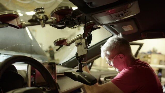 View from inside car of male workshop technician busy removing windshield