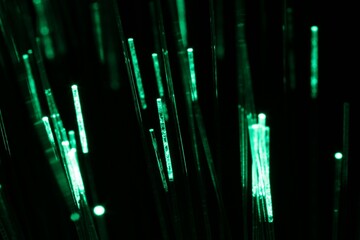 Optical fiber strands transmitting green light on black background, macro view