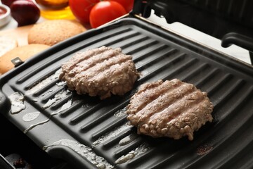 Delicious hamburger patties cooking on electric grill, closeup