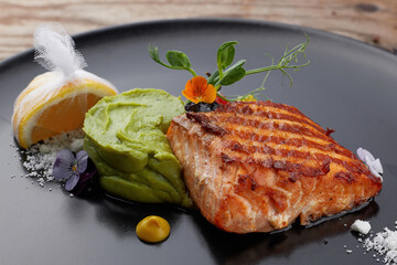 Piece of the fried salmon on a black dish with a lemon. steak. Filet