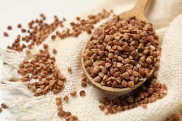 Spoon with dry buckwheat and white fabric on table, closeup. Space for text