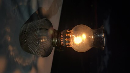 Flickering flame in vintage oil lamp casting shadow on table against twilight backdrop. Vacation in Greece. Summer vibes. Tavern on the beach. Vertical. - Powered by Adobe