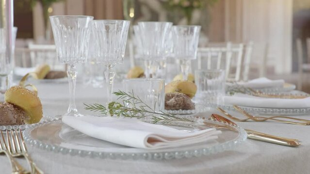 Slolw 4k orbit close up around beautifully decorated wedding dinner table with classy cutlery, glasses, bread and flower arrangement. Bright, light flooded big room in old italian style manor lodge