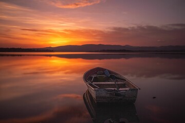 Wooden boat in a tranquil lake illuminated by the warm light of the setting sun
