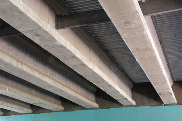 Architectural detail of concrete support beams beneath an overpass, with metal sheeting between the...
