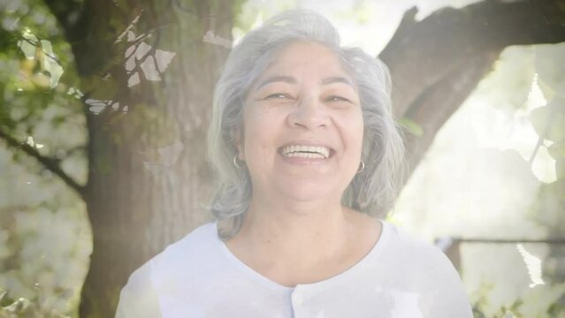 Animation of spots of light and trees over smiling senior biracial woman in garden