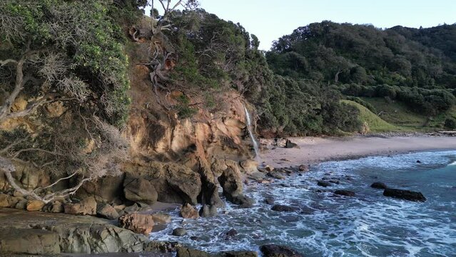 Beautiful coastal waterfall spills right onto rocky homunga beach, explore new zealands stunning coast