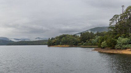 the view of a lake surrounded by trees and mountains from a distance