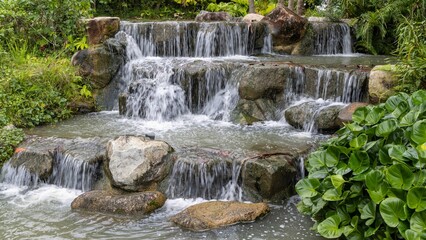 the small waterfall at the garden is running very fast over large rocks