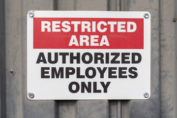 A caution sign reading “restricted area authorized employees only” bolted onto a metal plate...