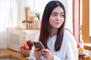 Happy Asian woman holding smartphone and looking sideways, smiling happily with the phone message she received