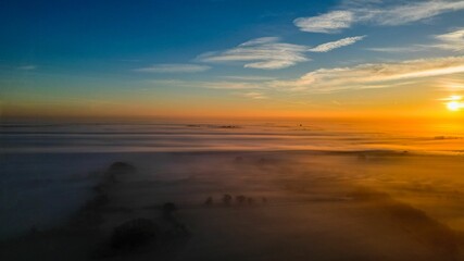 Aerial view of breathtaking landscape of the sun setting behind a rolling blanket of fog