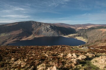 Fototapeta na wymiar Stunning view of the Lough Tay lake surrounded by lush vegetation under the cloudy blue sky