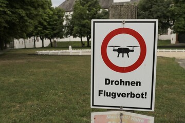 White rectangular sign with red and black text reading 'Drones flight ban' in German beneath it