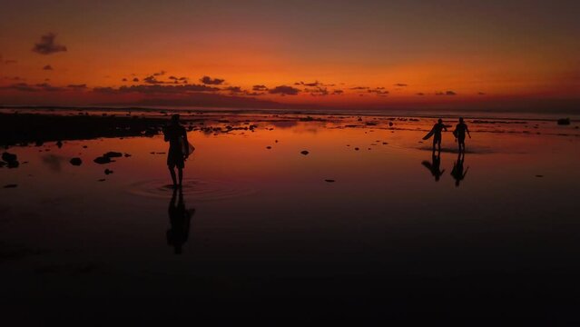 Silhouette view of three surfers walking on the beach with their surfer boards at sunset