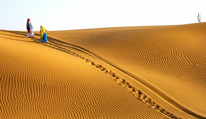 two people standing in the desert while carrying onto the dune