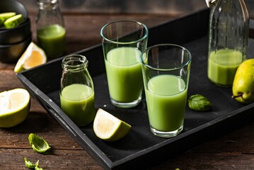 Closeup of green smoothie glasses with fruits and vegetables on a wooden surface