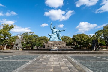 Peace Statue in the Peace Park, Nagasaki surrounded  by lush trees - obrazy, fototapety, plakaty