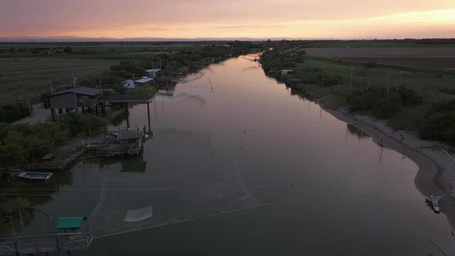 Descending drone of fishing huts on shores of Estuary at sunset near Comacchio Valley, Italian