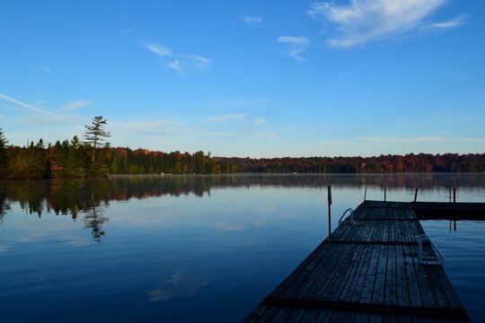 Idyllic image of an empty dock on a tranquil lake surrounded by lush trees in the fall season