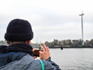 Man dressed in winter clothing stands on the beach, camera in hand, capturing the scenic view