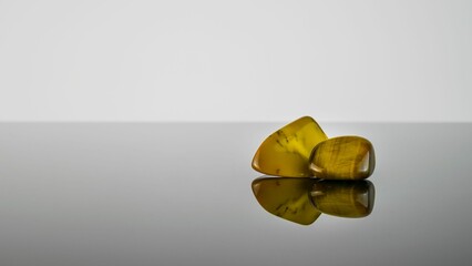 Amber rock crystals with their reflection against a grey background.