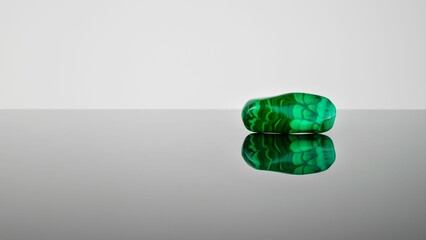 Green jade rock crystal with its reflection against a grey background.