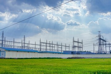 Fototapeta premium Grassy landscape dotted with power lines with towering structures in the industrial area