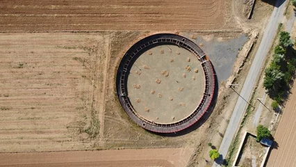 Fotobehang View of Plaza de toros de Villarquemado circular structure in the middle of a vast empty field © Wirestock