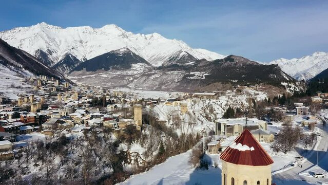 Aerial drone camera shot of Mestia village in Svaneti region, Georgia, Caucasus mountains. Winter sunny day, Main church with red roof