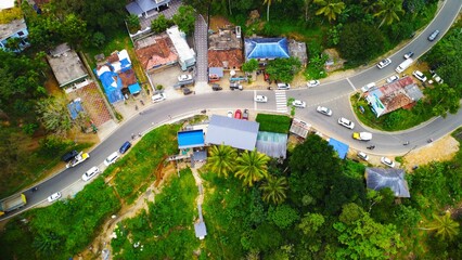 Aerial view of a road with cars surrounded by green trees and residential buildings. Munnar, India.