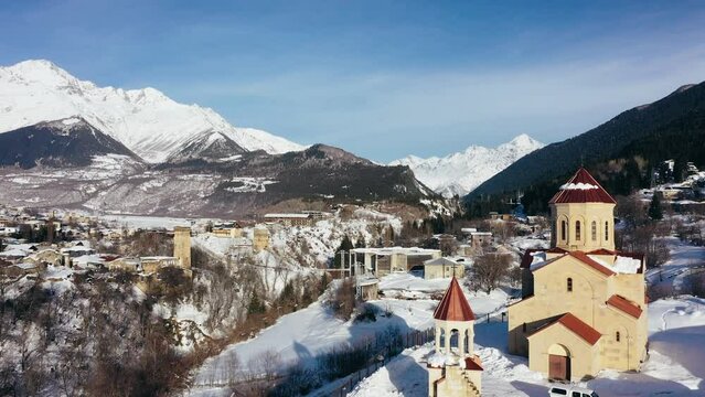 Aerial drone camera shot of Mestia village in Svaneti region, Georgia, Caucasus mountains. Winter sunny day, Main church with red roof
