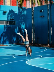 A vertical shot of a young female in shorts doing a handstand on a basketball field
