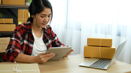 Fototapeta na wymiar Woman checking stock goods supply delivery package shipping use document checklist. Asian woman startup small business at home office. Online entrepreneur asian woman use tablet checking online order
