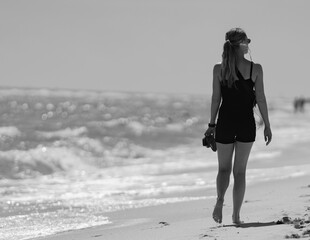 a greyscale back view of a female walking at the beach