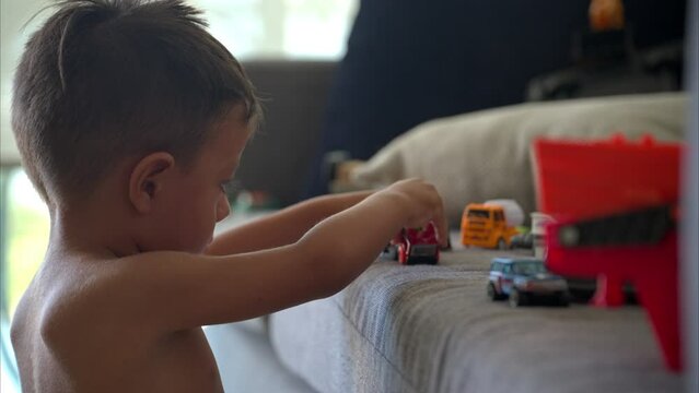 Close up of a young shirtless hispanic boy focused concentrated playing with his car toys. Creativity and imagination concept. Slow motion