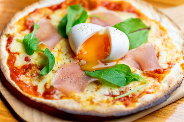 とろりとした半熟卵の黄身と生ハム、ルッコラを贅沢にのせた、香ばしいクリスピービスマルクピッツァ。しっとりした質感の具材が際立つ一枚で、バルのメインやランチ、パーティー向けの販促に最適な高品質素材です。 | Crispy Bismarck pizza topped with a soft-boiled egg and prosciutto.