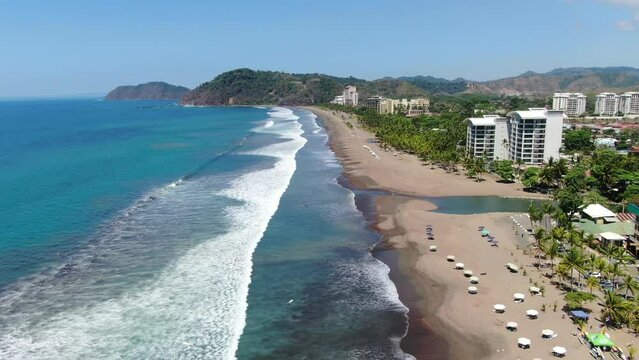 Costa Rica beach drone view showing sea, shore and forest on a sunny day over the pacific ocean in Jaco. Fly over in parallel to the shore