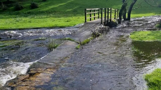 Jib shot of rustic stone submerged pathway leading to arched wooden bridge overflowing flooded river