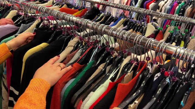 Hands of woman browsing through fast fashion store clothing rack