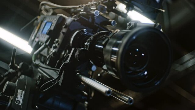 Low angle shot of a professional cinema camera and long telephoto zoom lens, remote device is turning the gears and the lens element is moving to change focal length. Focus on zoom motor.