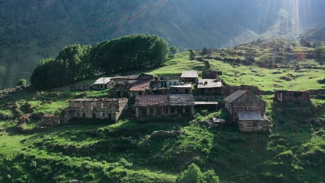 Abandoned village on green slopes of high mountains. Aerial view, drone video