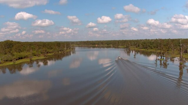 Aerial Backward Shot Of Motorboat In Atchafalaya River Amidst Green Landscape Under Cloudy Sky - Bayou, Louisiana