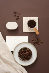 Brown roasted coffee beans on ceramic dishes decorated with white bricks podiums and beige fabric on dark brown background. Minimal scene for advertising organic product for body care