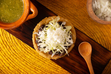 Sope. Traditional homemade Mexican food prepared with flattened and pinched on the border fried corn dough covered with refried beans, green or red sauce, lettuce, cheese, onion and sour cream.