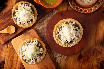 Sopes. Traditional homemade Mexican food prepared with flattened and pinched on the border fried corn dough covered with refried beans, green or red sauce, lettuce, cheese, onion and sour cream.