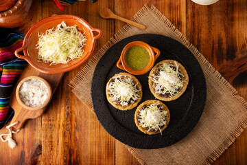 Sopes. Mexican typical food prepared with flattened fried corn dough covered with refried beans, green or red sauce, lettuce, cheese, onion and sour cream. Served on stone comal plate.