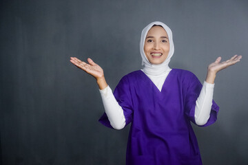 Asian hijab nurse wearing purple medical uniform pointing or showing on her right side. Design for...