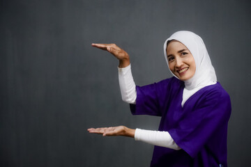 Asian hijab nurse wearing purple medical uniform pointing or showing on her right side. Design for...
